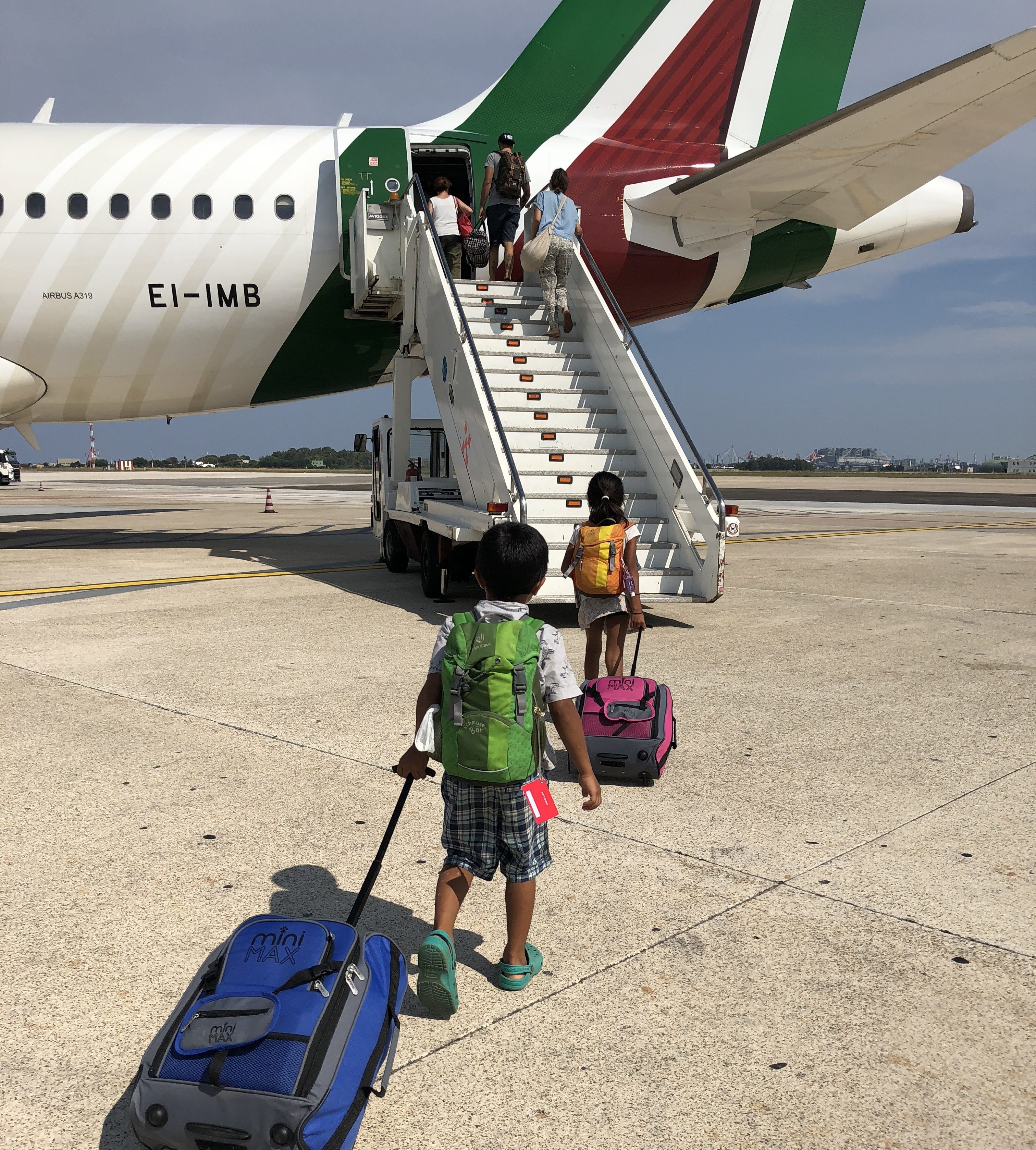 two kids travelling, suitcases and backpacks, boarding a plane from tarmack